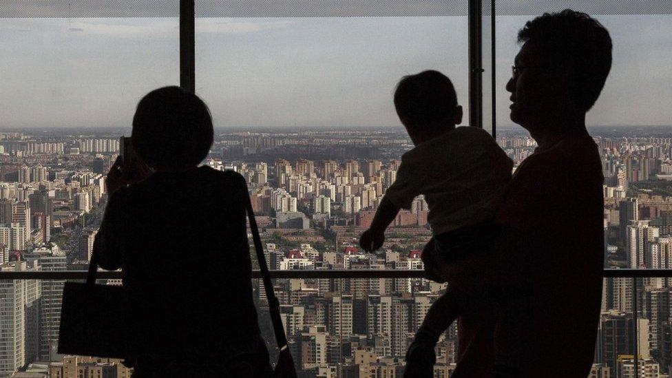 A Chinese couple stand with their child as they look out on residential and office buildings from a luxury hotel on June 11, 2015 in Beijing, China.