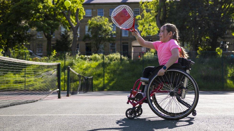 kid playing tennis in a wheelchair on an outdoors tennis court