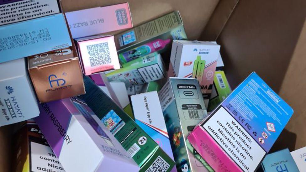 A close-up of packets of cigarettes and vapes in various colours