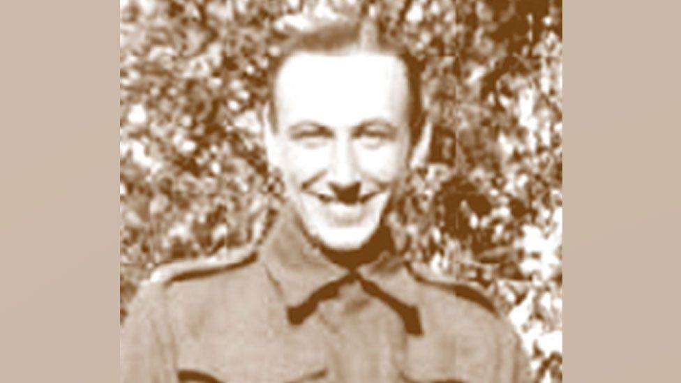 A sepia-toned black and white image of Tom Allard. He has short hair and is wearing a British Army tunic. He is smiling broadly.