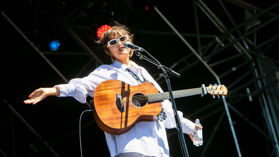 A young woman with a guitar stands on a stage