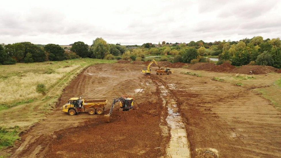 Two yellow diggers work on a large area of mud surrounded by trees