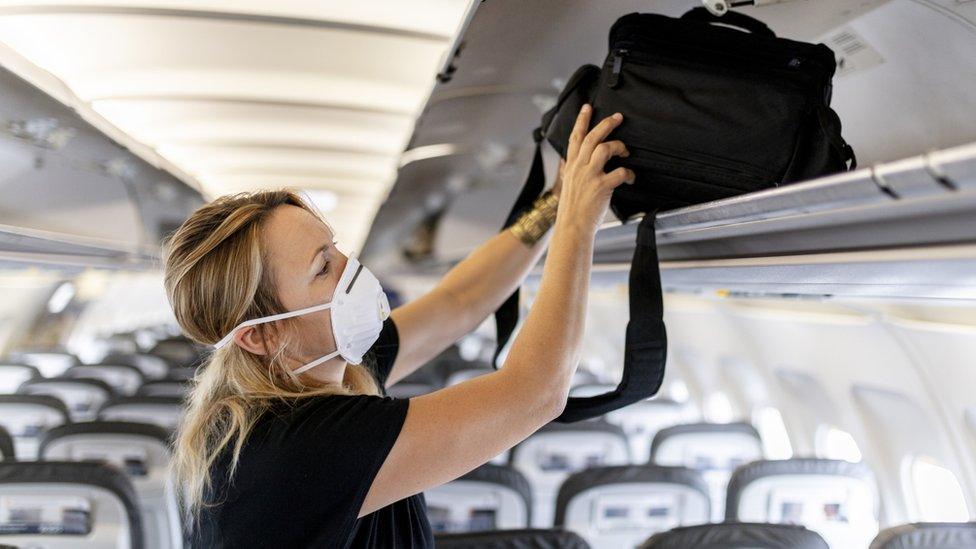 Woman putting luggage in overhead locker