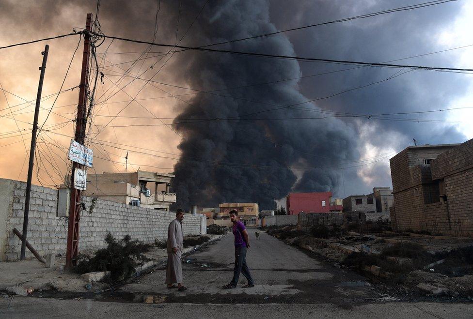 Local men pictured after an oil field was set on fire by retreating IS fighters ahead of the Mosul offensive burns behind them on October 21, 2016 in Qayyarah, Iraq.