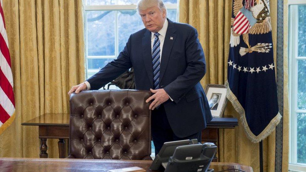 Donald Trump poses behind his desk in the Oval Office.