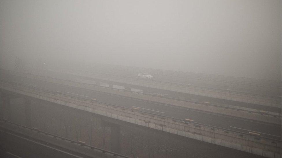 A car drives along a highway on a polluted day in Beijing on December 1, 2015. China has ordered thousands of factories to shut as it grapples with swathes of choking smog that were nearly 24 times safe levels on December 1, casting a shadow over the country's participation in Paris climate talks. A thick grey haze shrouded Beijing, with the concentration of PM 2.5, harmful microscopic particles that penetrate deep into the lungs, climbing as high as 598 micrograms per cubic metre