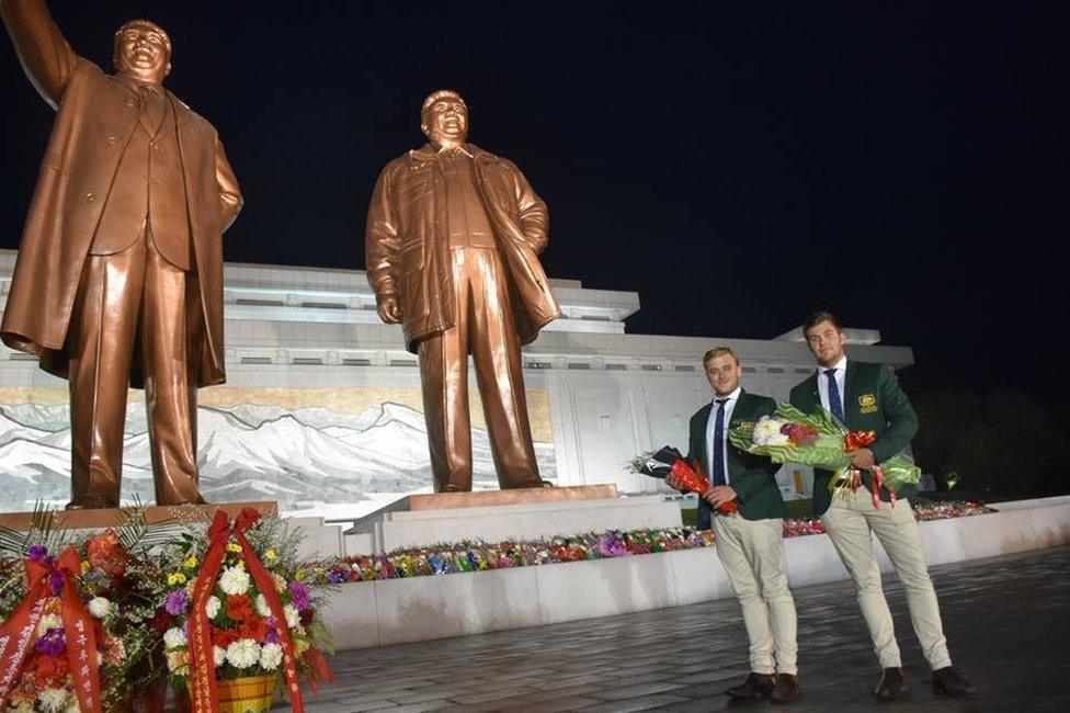 Two Australians pose for a photo in front of a monument in North Korea