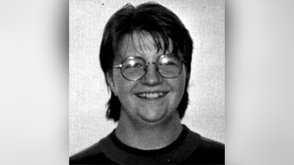 Black and white headshot of a woman smiling at the camera wearing round glasses.