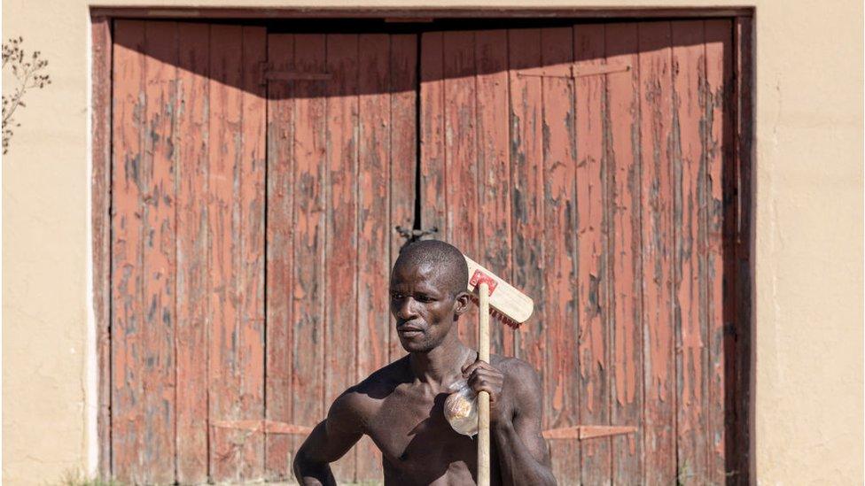 Khotso, poses for a portrait as he carries his broom while looking for odd jobs in Koffiefontein on May 22, 2024