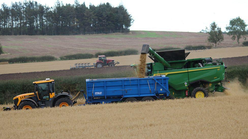 Two tractors head in different directions - one of them large in the foreground and the other more distant.