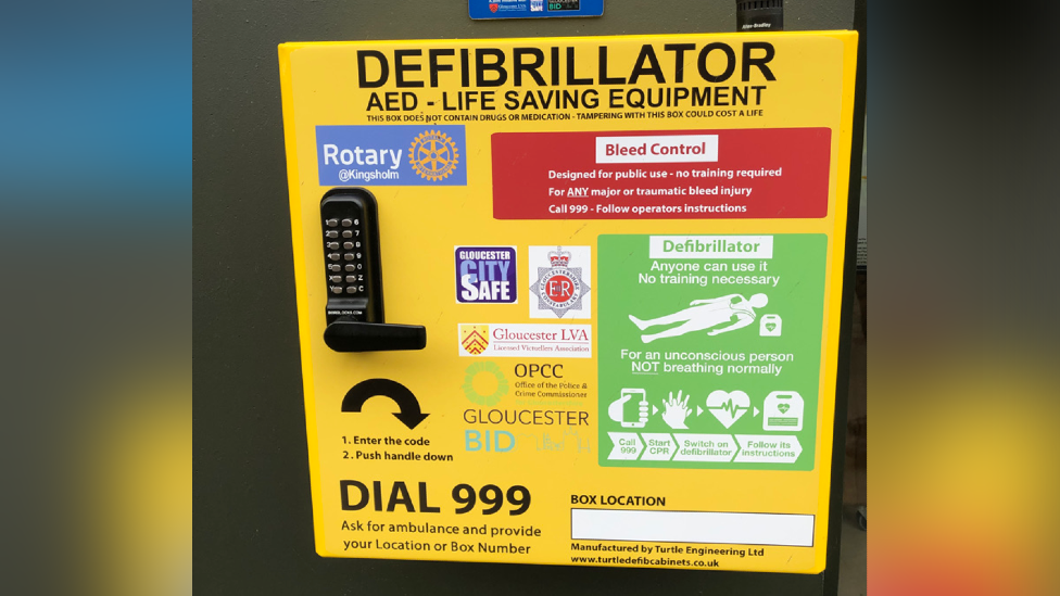 Defibrillator in Gloucester. It is bright yellow, with black text saying Defibrillator. There is a key code on the left and information about how to use it.