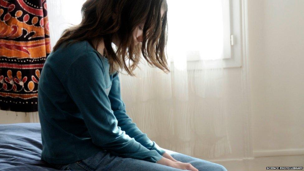 A young girl sitting on a bed, looking sad