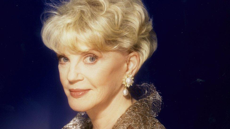 Judith Krantz wearing a gold shirt and pearl earrings