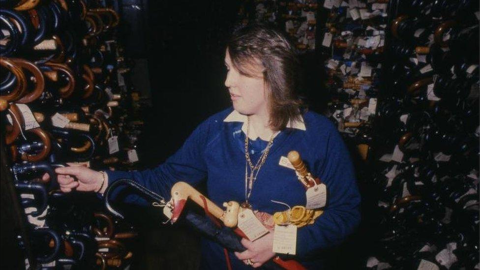 A lost property office attendant sorts through hundreds of umbrellas in 1983, from London Transport Museum's collection