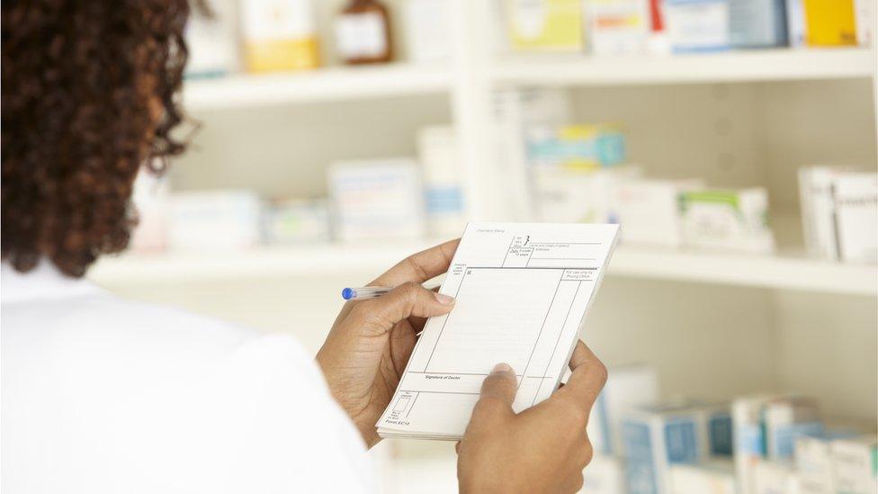 A pharmacist looks at a prescription in front of shelves of medication