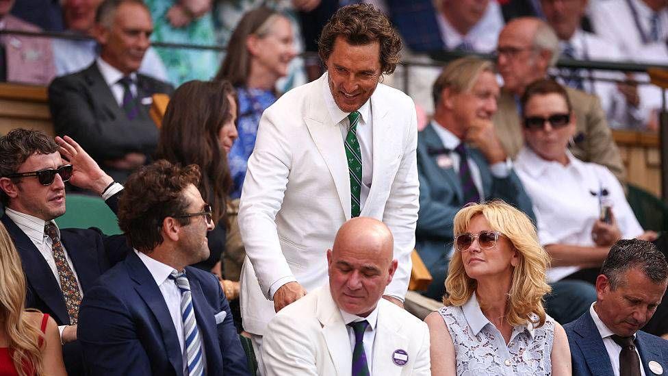 US actor Matthew McConaughey speaks with US former tennis player Andre Agassi as he arrives on the royal box on Centre Court. The US actor wears a white suit, and Agassi wears a navy blue suit.