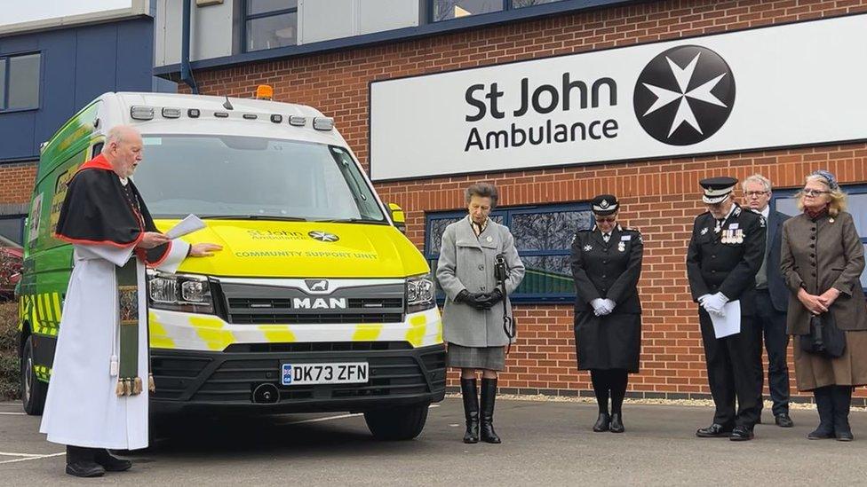 The Princess Royal stands to the right of the green and yellow vehicle, with a clergyman on the left, they are joined by people in uniform