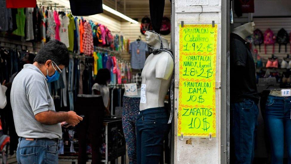 A man uses a mobile phone in front of a sign displaying prices in US dollars outside a clothing store in Caracas on December 9, 2020