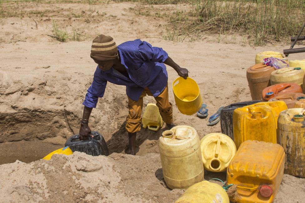 A man collects water on Kikuu River. During the rainy season, water percolates into the sand and is stored underground. Then during the dry season, locals dig small wells in the sand to get water