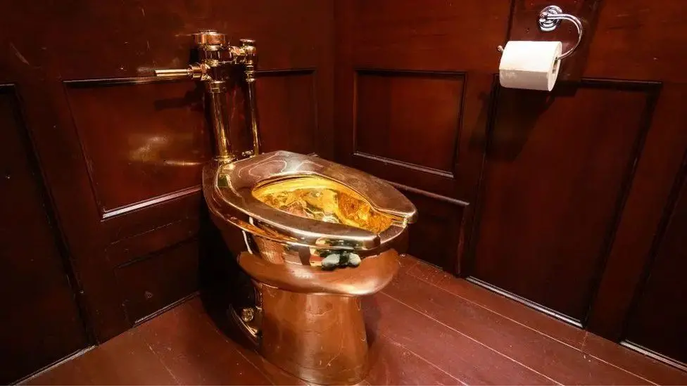 A general view of the golden toilet, which is plumbed into a wooden-panelled room.