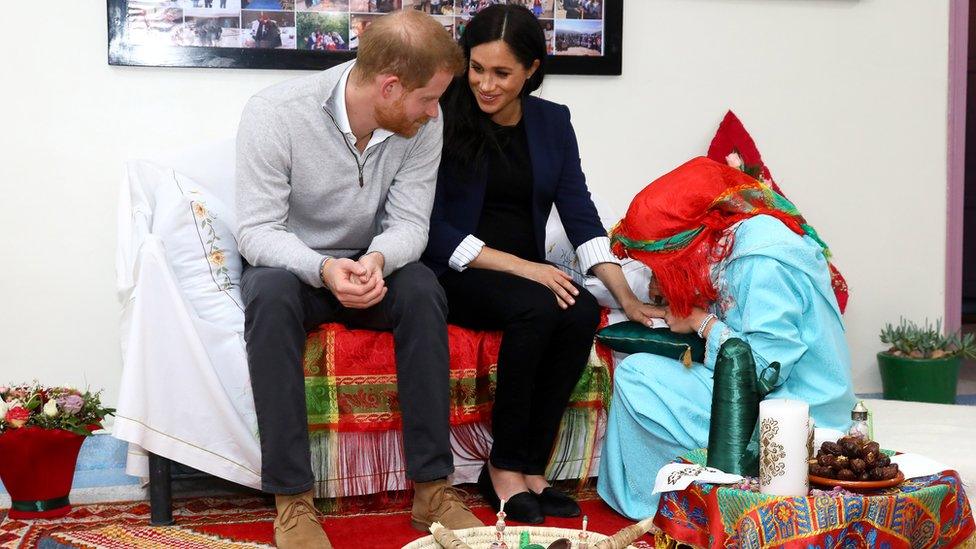 The Duchess of Sussex sits with Prince Harry as henna is applied to her hand