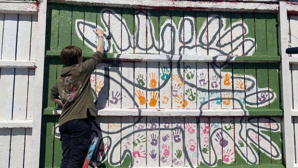 An artist paints a white design on a green background for Bristol Women's Voice on billboards on the M32