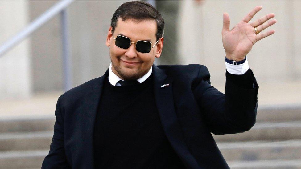 George Santos in sunglasses, sweater, dark blazer, waving