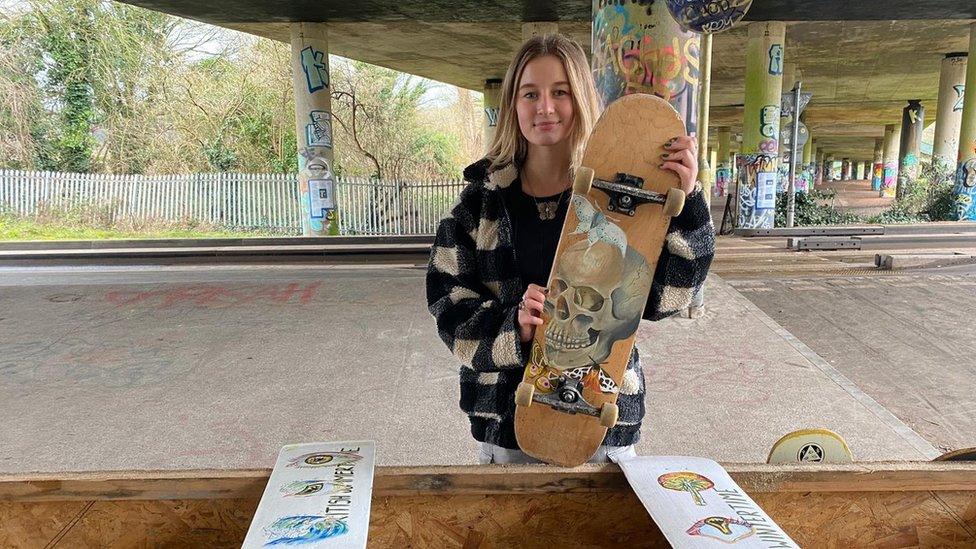 16 year old Ruby Parker holding up a skateboard featuring one of her painted designs