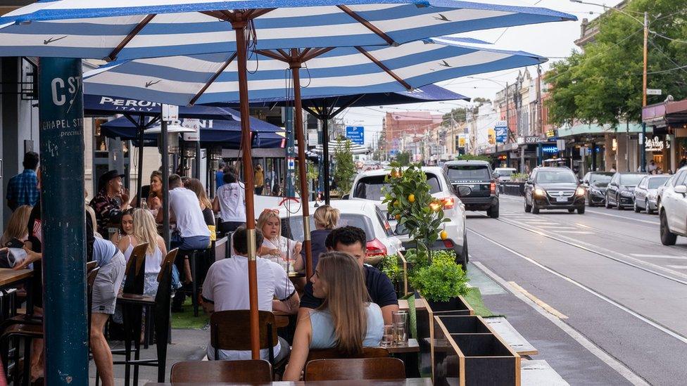 People sit outside on cafe tables on Chapel St in Melbourne