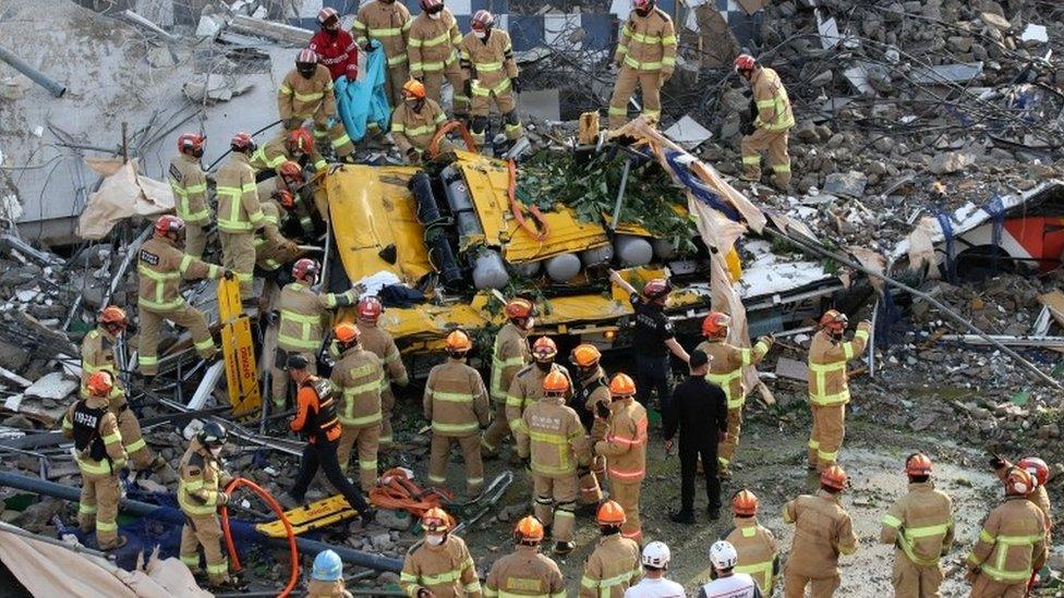 South Korean firefighters search for passengers from a bus trapped by the debris of a collapsed building in Gwangju