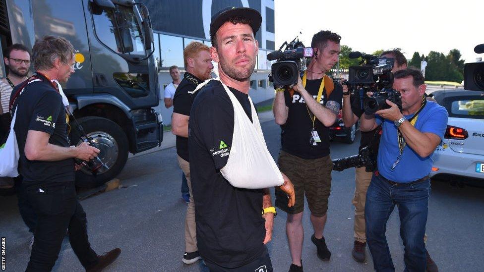 Mark Cavendish wearing a sling on his right arm while being filmed by camera crews