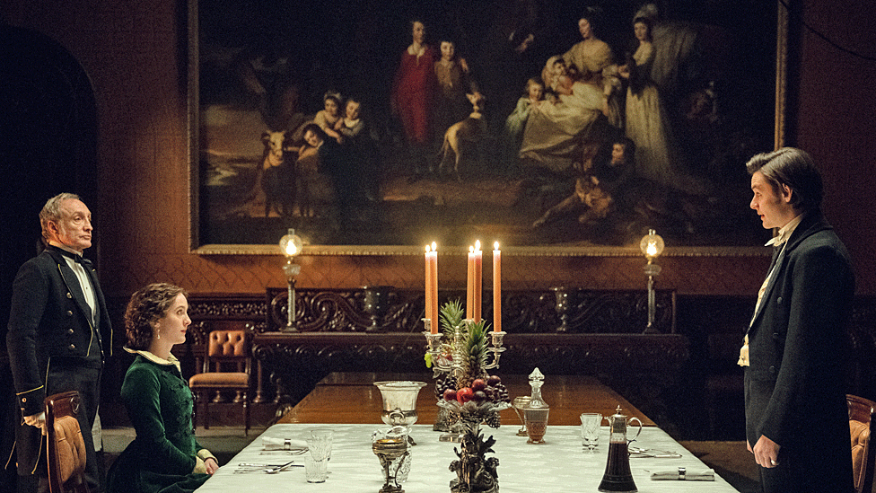 Michael McElhatton, Louis Partridge, and Ann Skelly in Penrhyn Castle dining room with candles on the table in House of Guinness