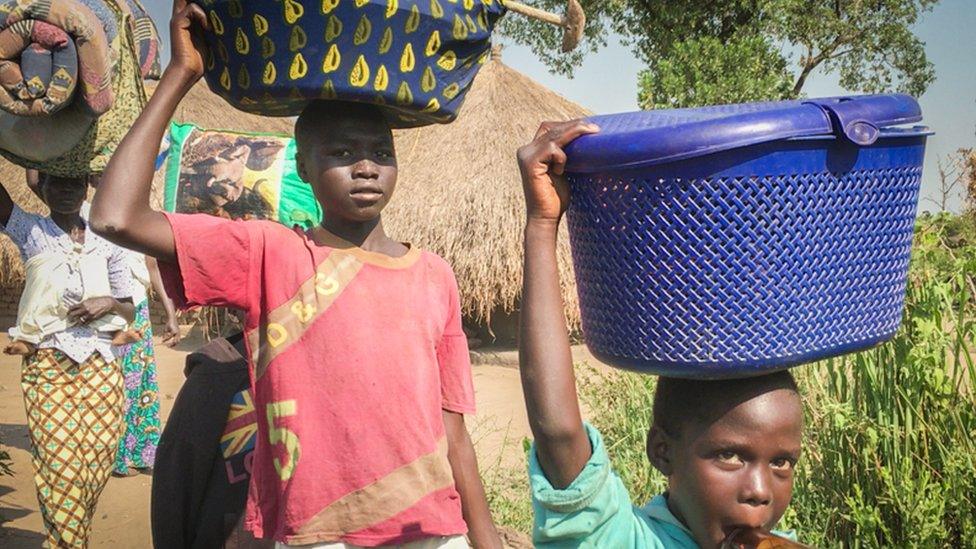 Refugees escaping on foot carry their belongings on their heads