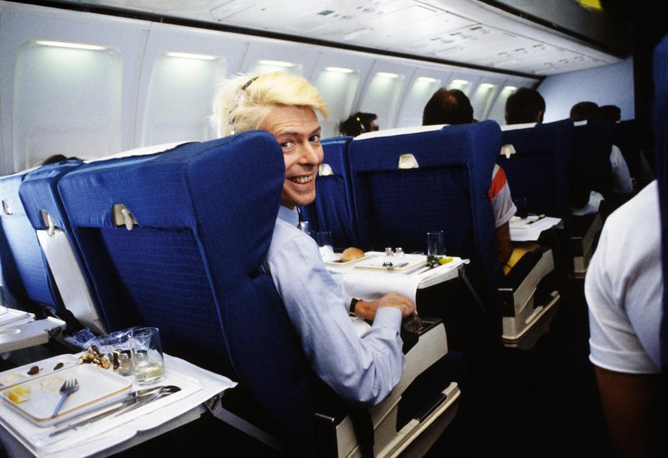 David Bowie on a commercial flight during the Australian leg of his Serious Moonlight tour.