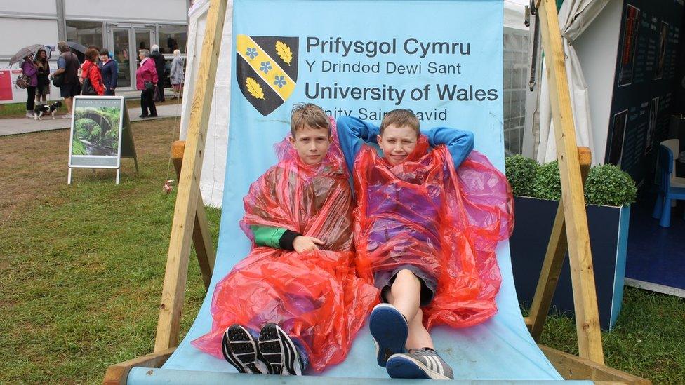 Dau fachgen ifanc yn eu cotiau glaw ar sêt haul // Two young children on an outsized deckchair - in anoraks