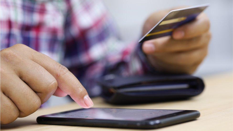 Closeup young man hands holding credit card and using smart phone for online shopping or reporting lost card, fraudulent transaction