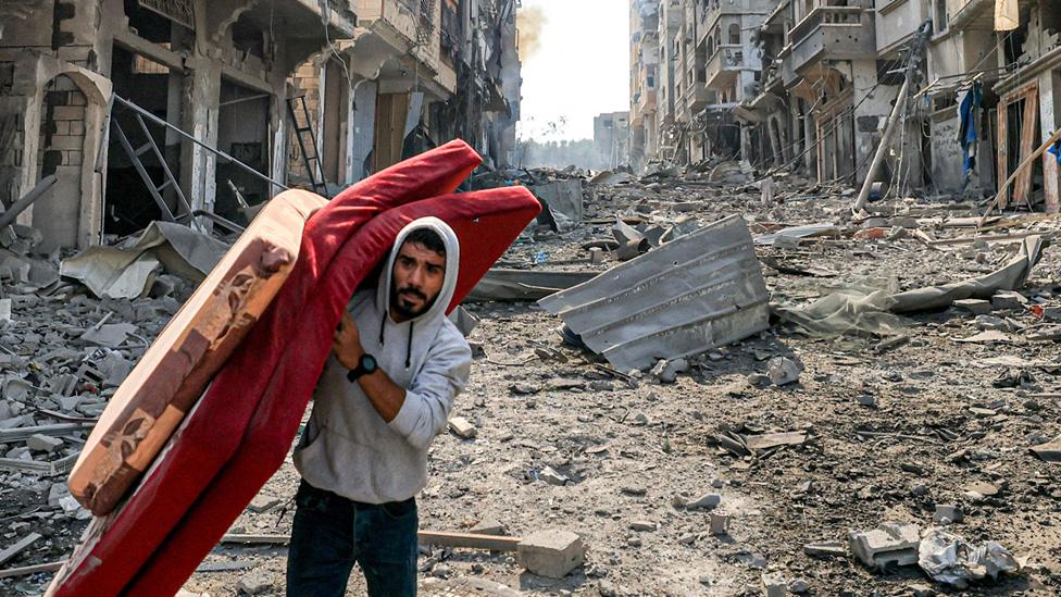 A man walks with mattresses through destruction in the Gaza Strip's Jabalia refugee camp