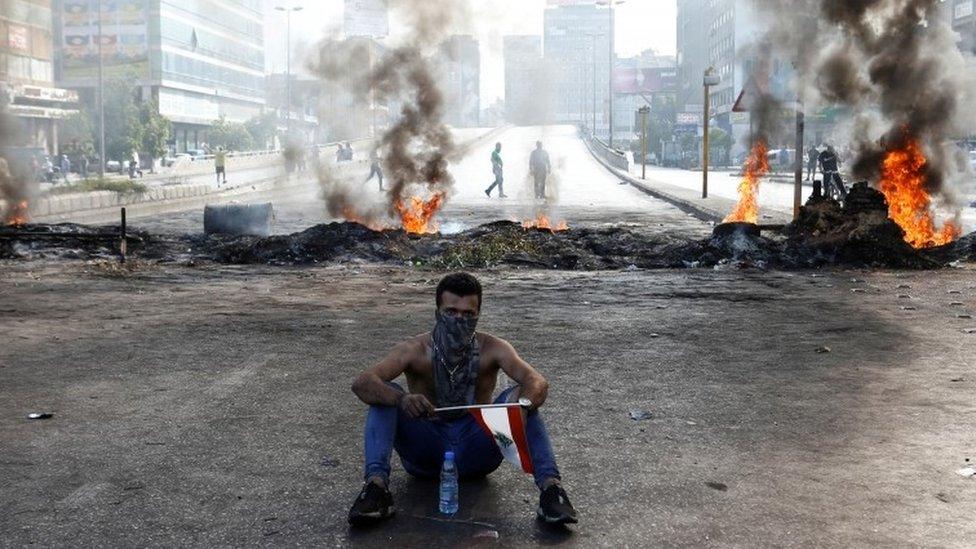 A protester sits in front of flames in Dora, Lebanon