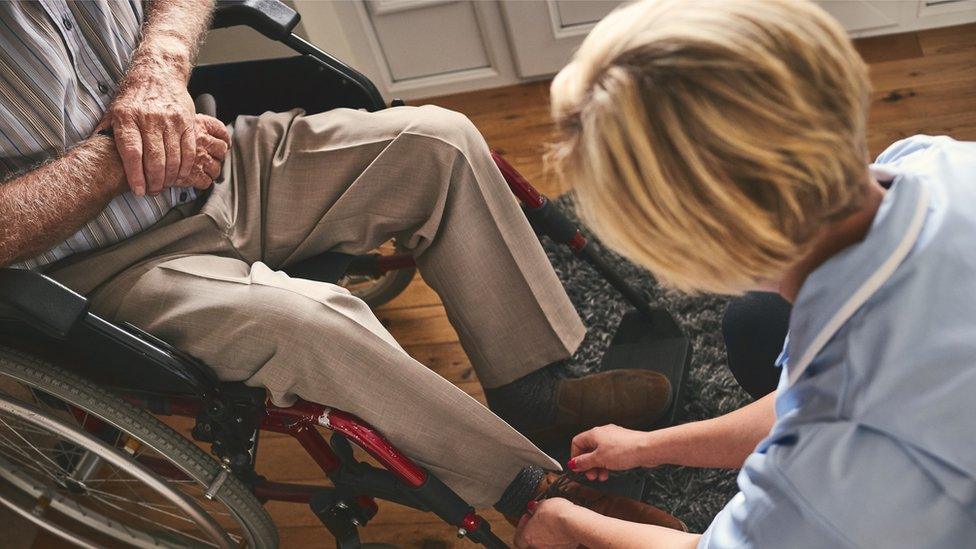 A care worker ties a man's shoelaces