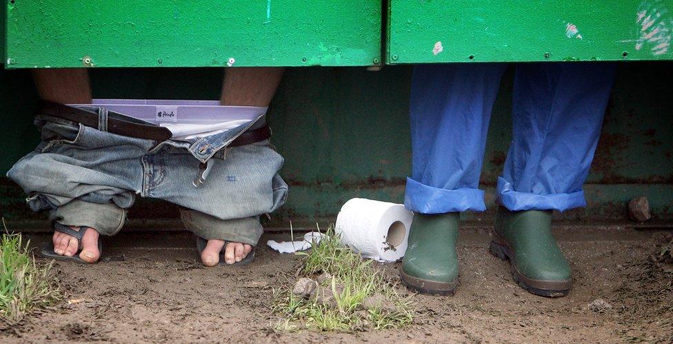 Festival goers (pictured with just their lower legs showing under a toilet door) use the toilets at Glastonbury Festival in Somerset, UK