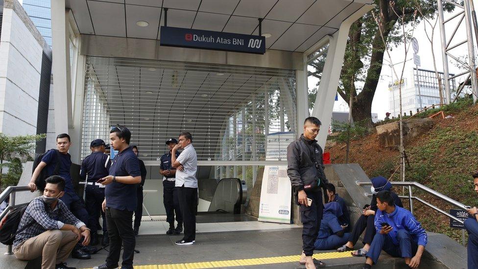 Train passengers wait by a station after a blackout in Indonesia