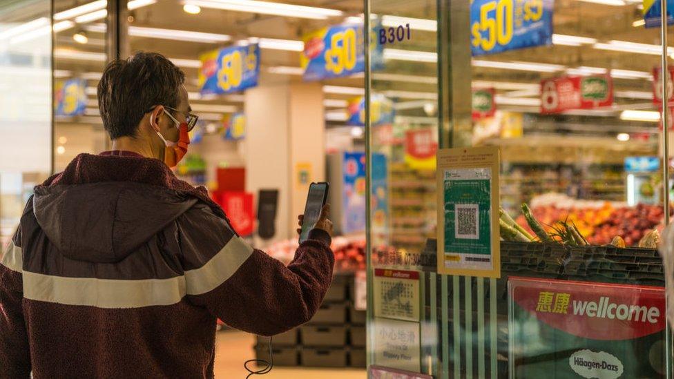 A man in a mask scans a vaccine pass QR code outside a shop in Hong Kong