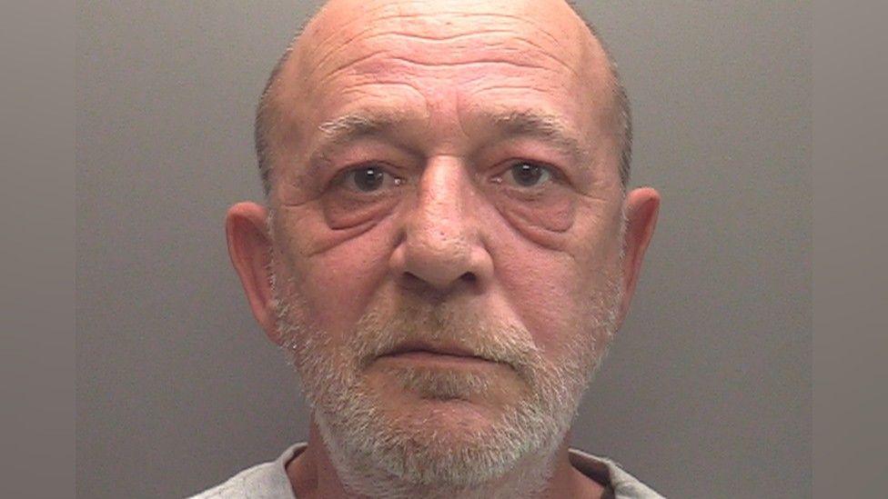 Police mugshot of Richard Admans looking directly at the camera. He has a grey stubbly beard and short grey hair 