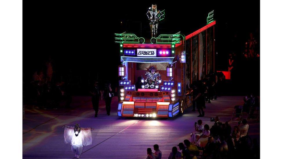 performers-in-costumes-covered-in-bright-lights-driving-a-colourful-bus