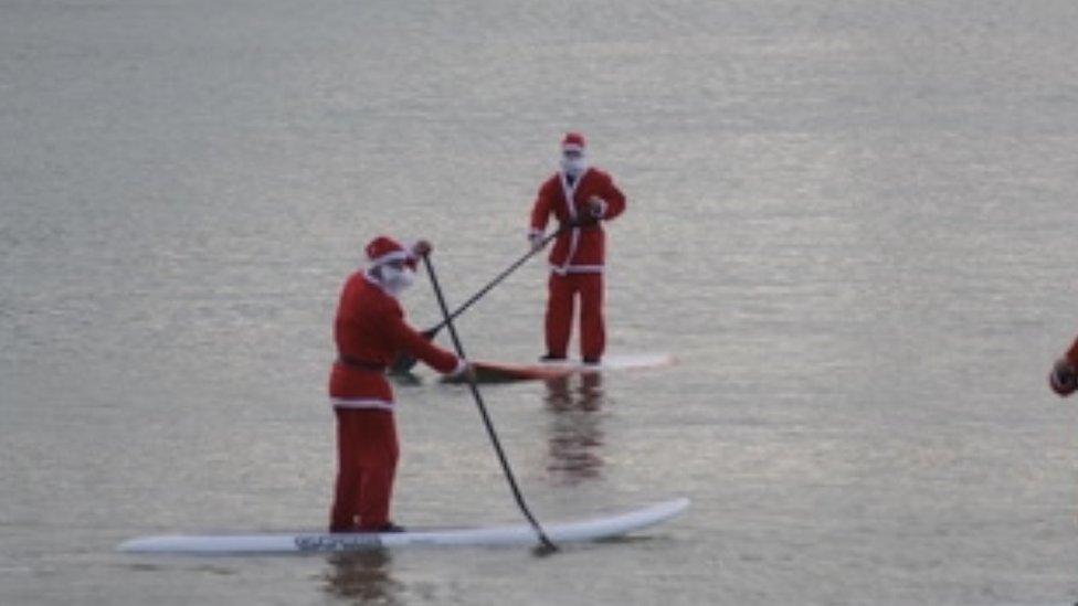 Two people dressed up as Santa on paddle boards in the sea