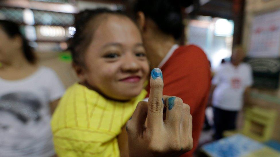 Fife Vanice Dayola, being held by her mother, shows her ink-stained finger to the camera, at a polling station in Davao city, on 9 May