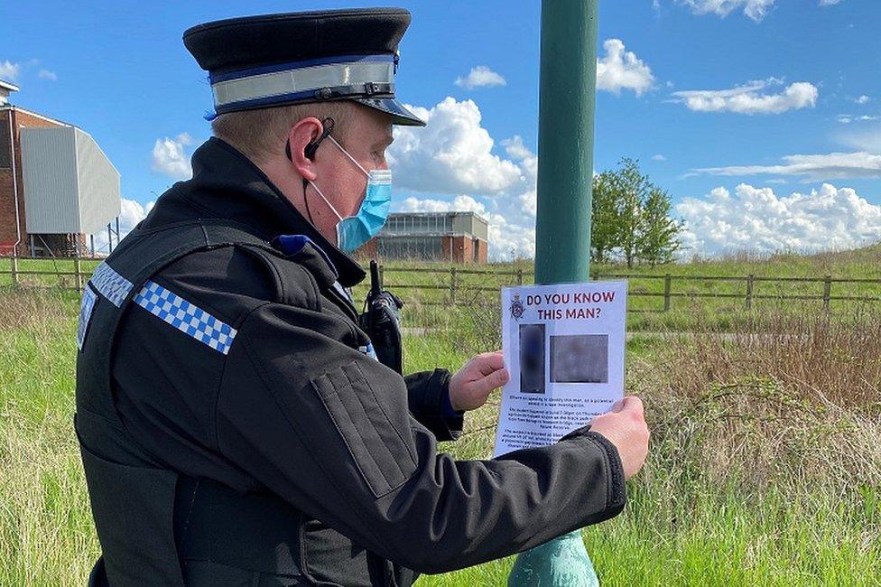 A police officer attaches a poster of the suspect to a lamppost