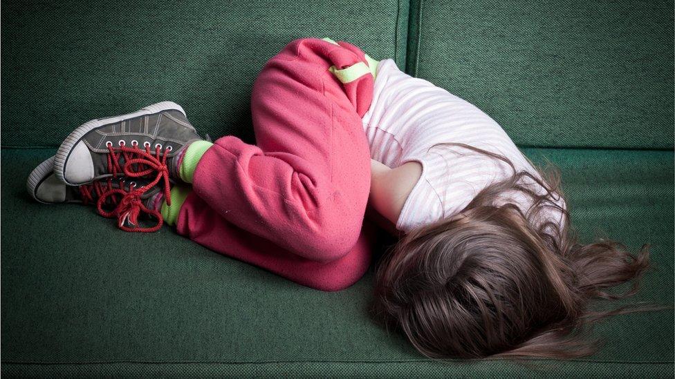 Child in foetal position on sofa.