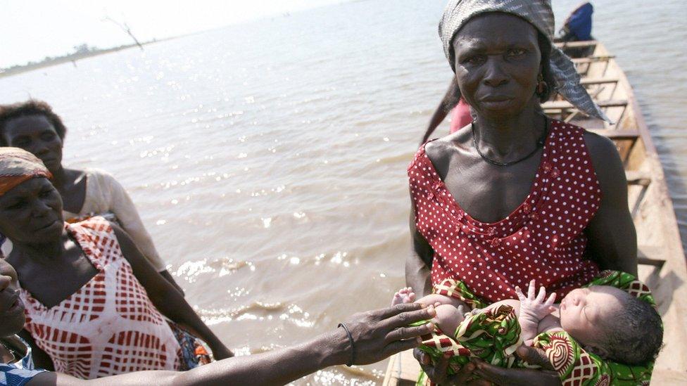 A woman holds a new-born baby, 11 April 2006, aboard a pirogue during a crossing of the Lake Volta