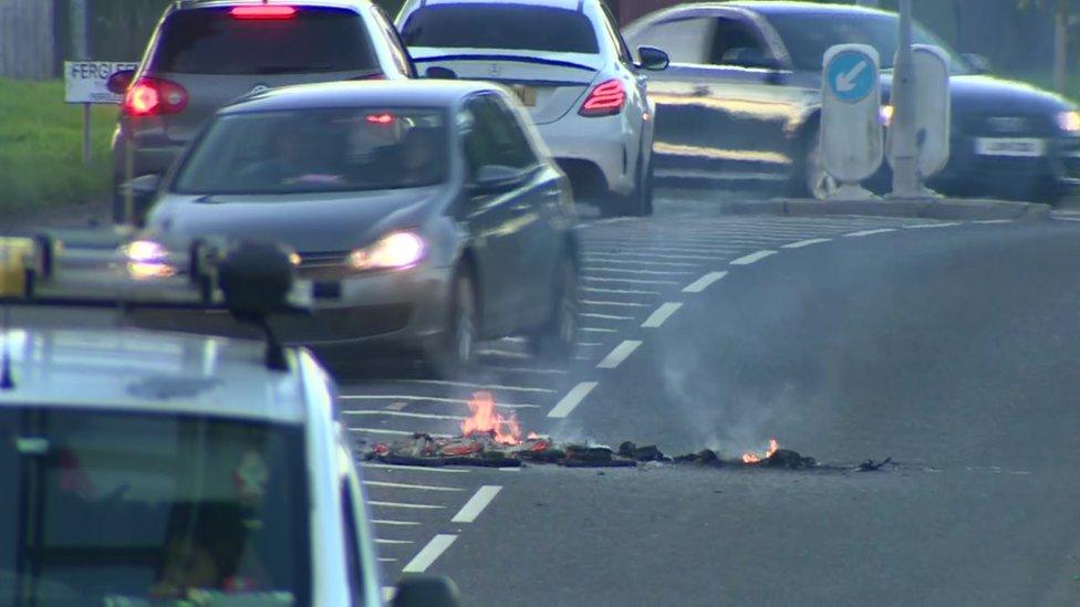 Cars drive past burning debris on a road in Galliagh in Londonderry